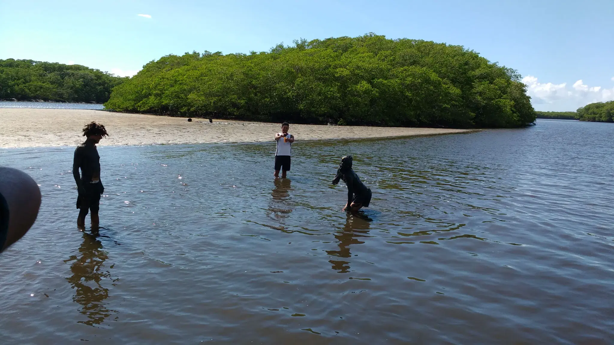 Banhistas em água rasa no rio Buranhém, com ilha de mangue ao fundo, em Porto Seguro